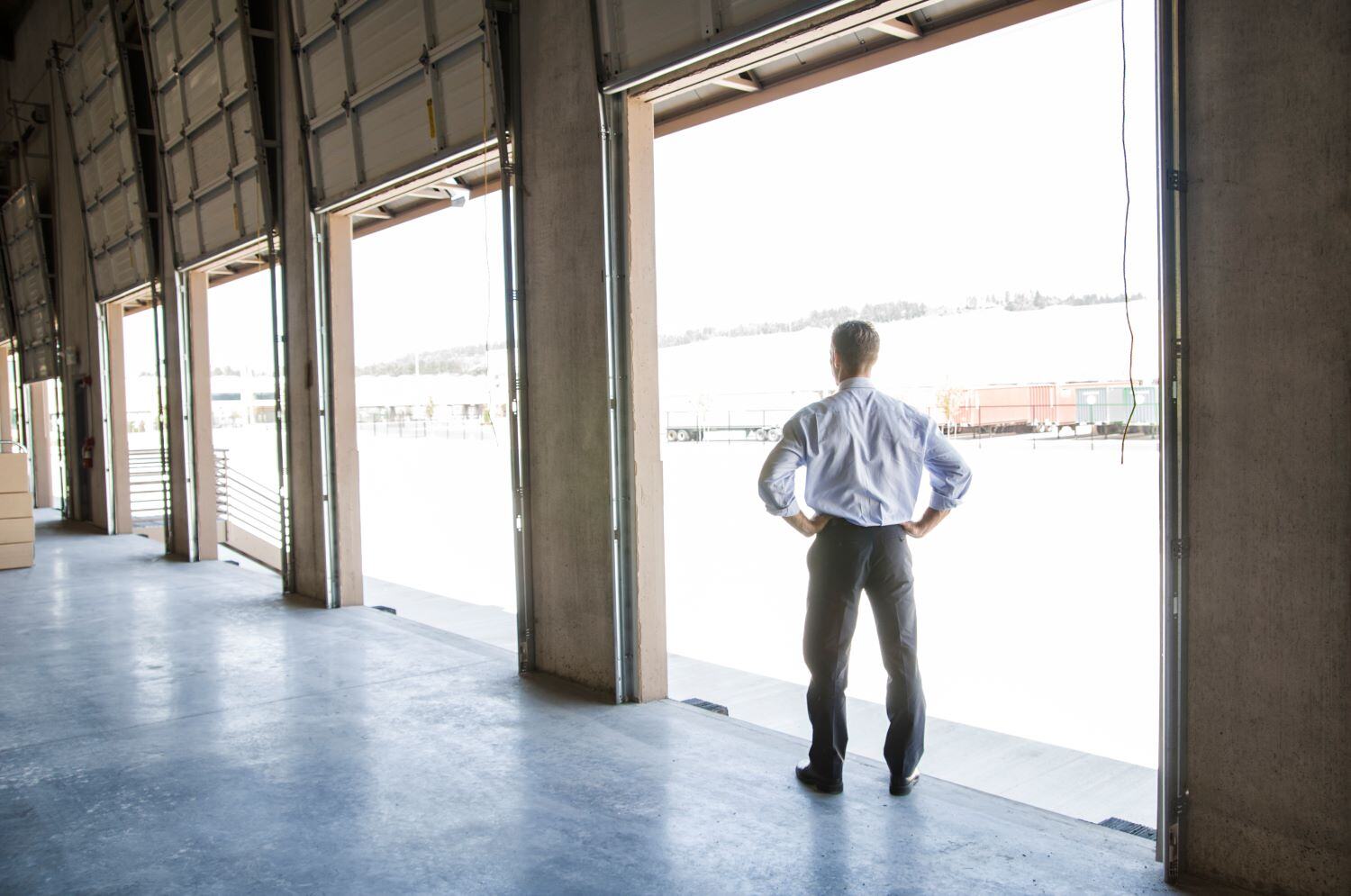 Young business man in dress shirt standing at the edge of a loading dock with hands on his hips and  his back to the camera,