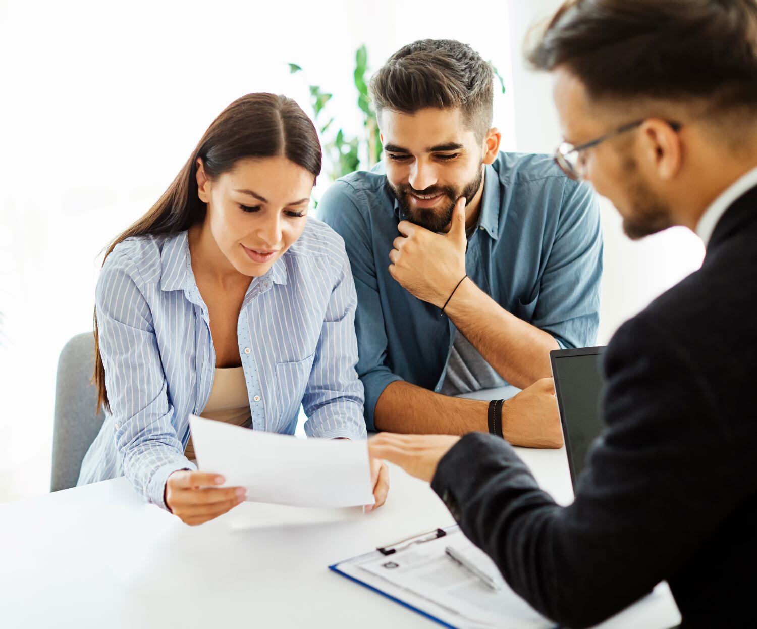 Young hispanic woman and man at a desk, reviewing a document and listening to a young man in a suit and glasses explain the information