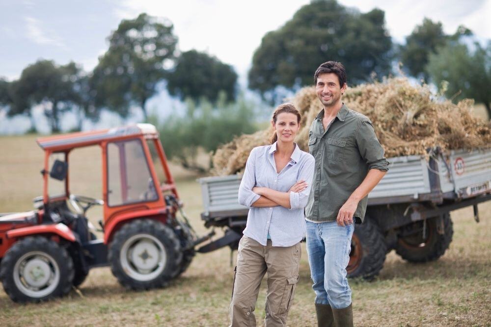 young white woman and man farmers in front of farm equipment