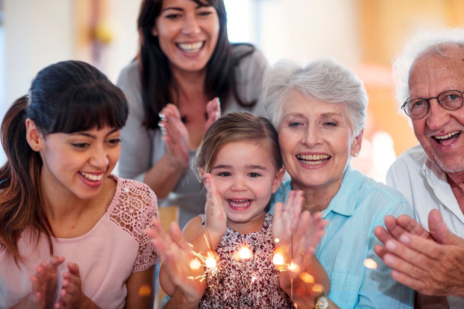 Multi-generational Hispanic family celebrating a little girl's birthday, blowing out candles on a birthday cake