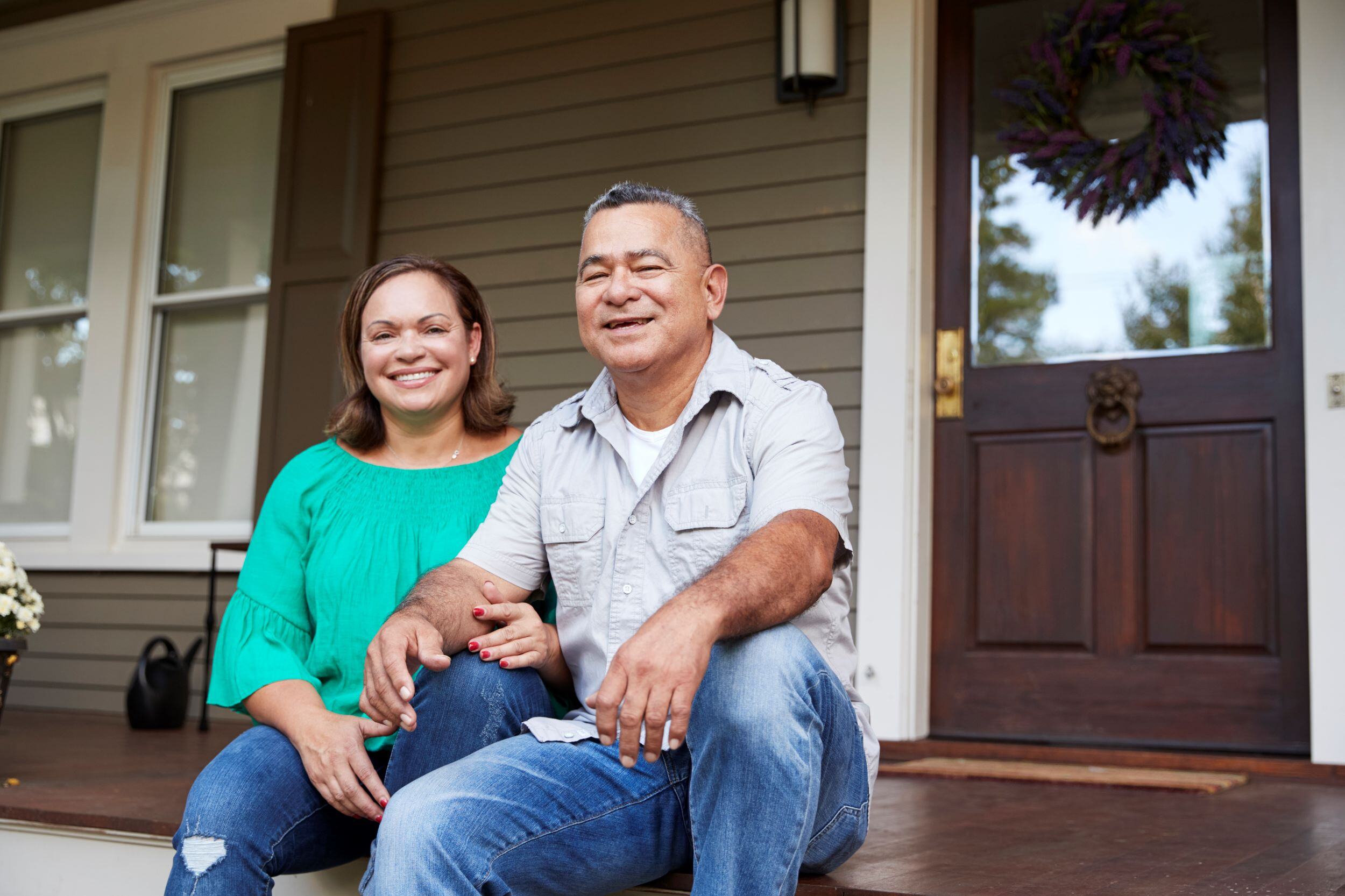 Happy, smiling, middle-aged Hispanic couple sitting on front stairs of a home.