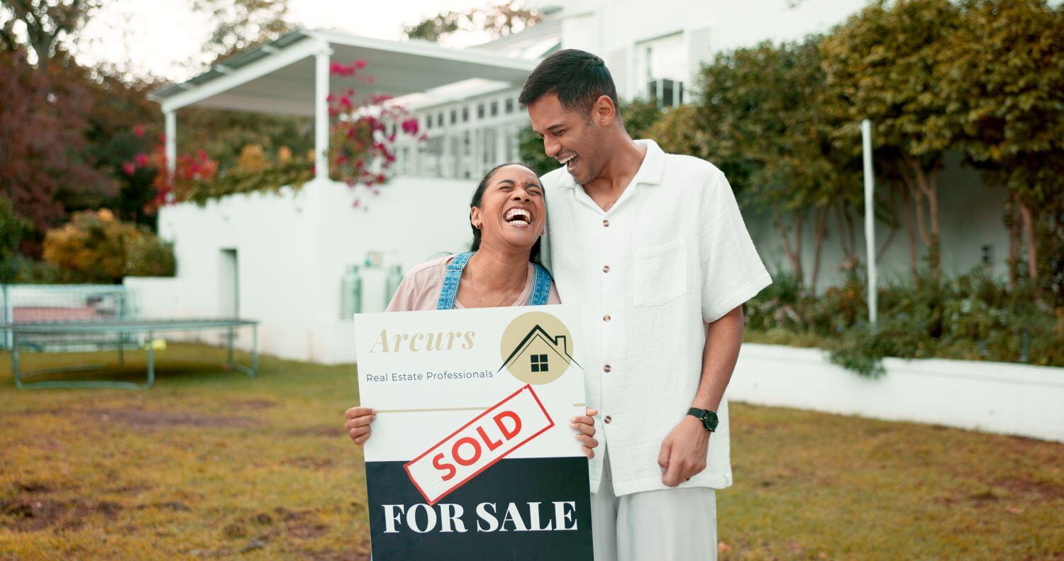 Young couple laughing and holding a Sold real estate sign