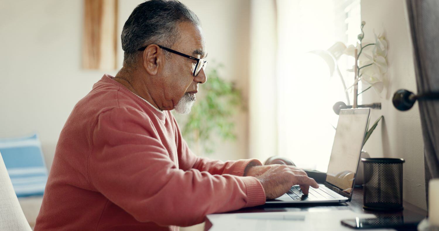 Older gentleman sitting at a desk working on a laptop