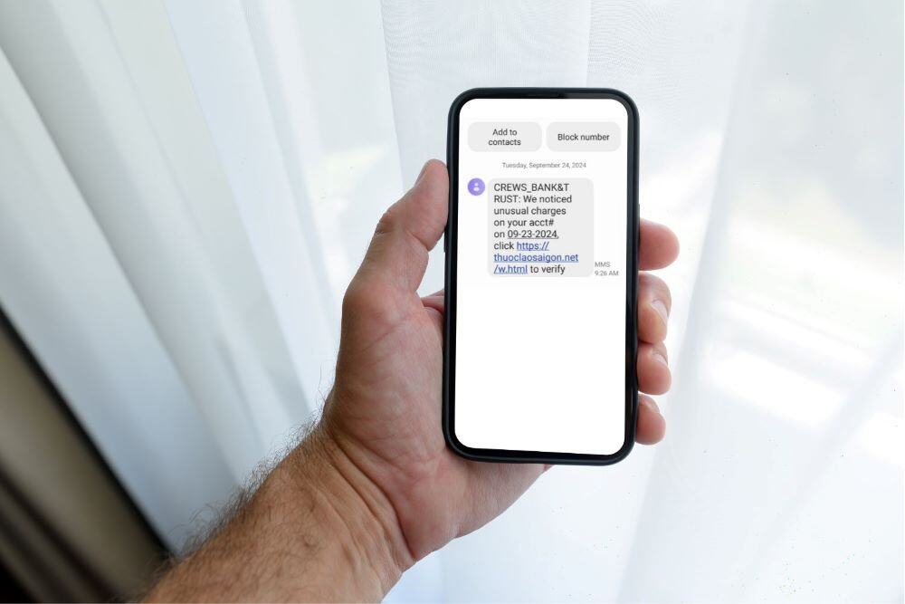 Man's hand holding a cellphone which is displaying a smishing text.