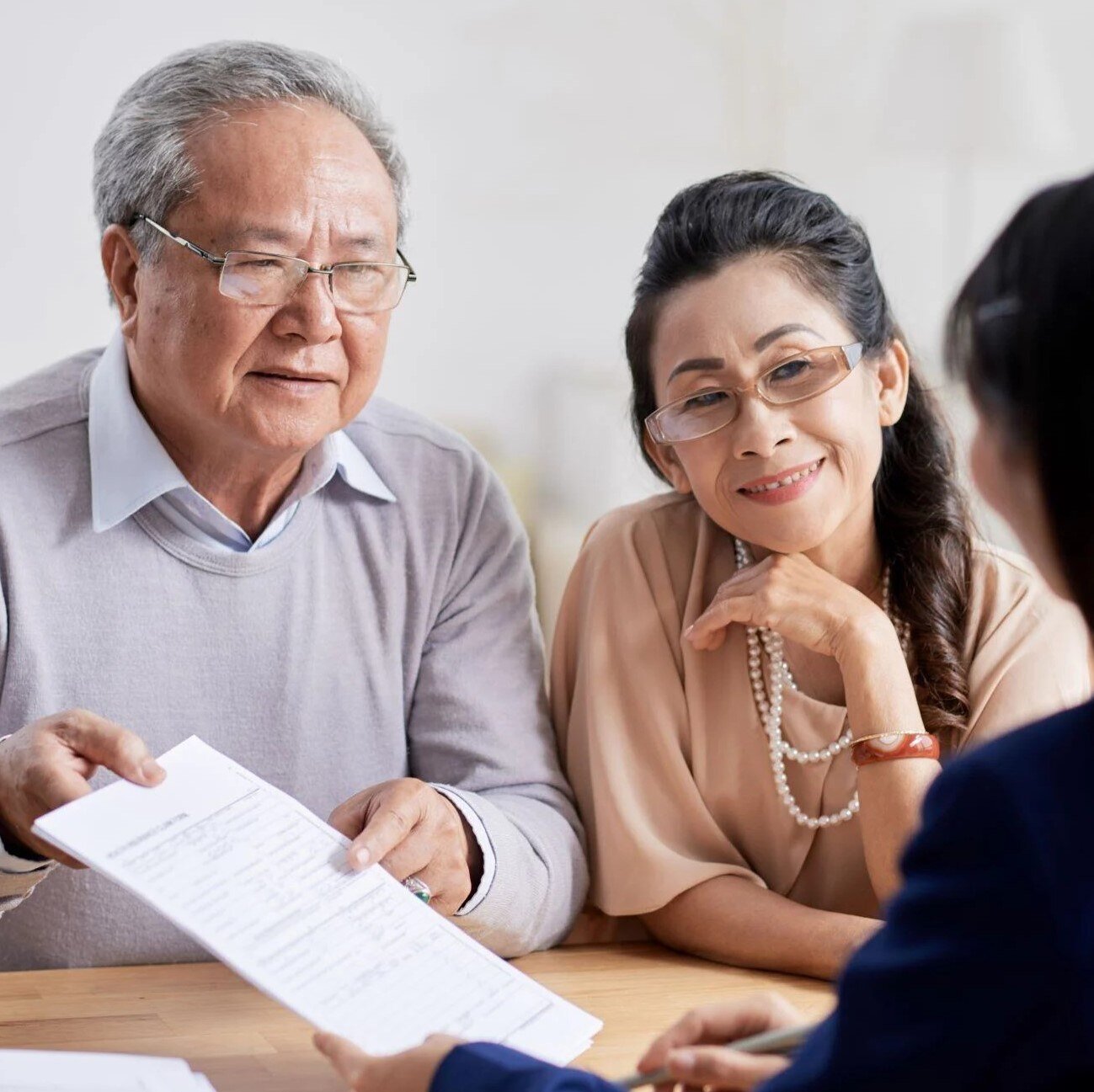 Older Asian couple sitting with a trust officer reviewing their estate planning documents.